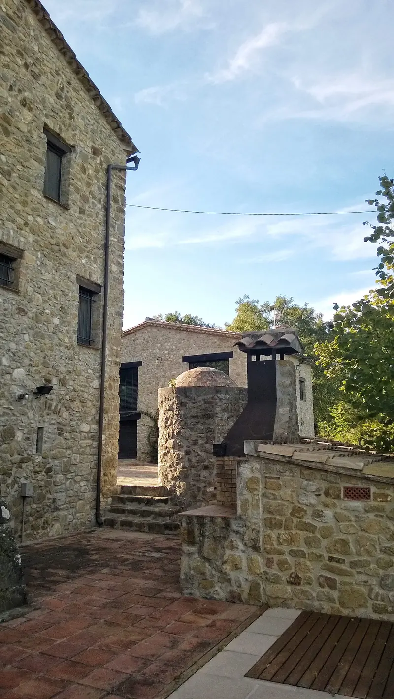 Pati estret entre construccions de pedra, amb paviment de rajola i una xemeneia