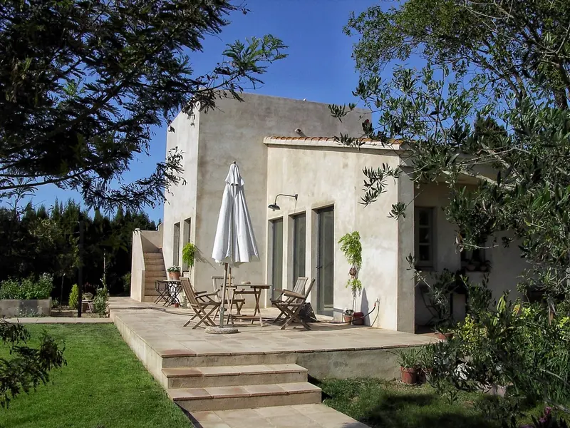 Casa d’estuc clar amb terrassa, para-sol i jardí envoltat d’arbres