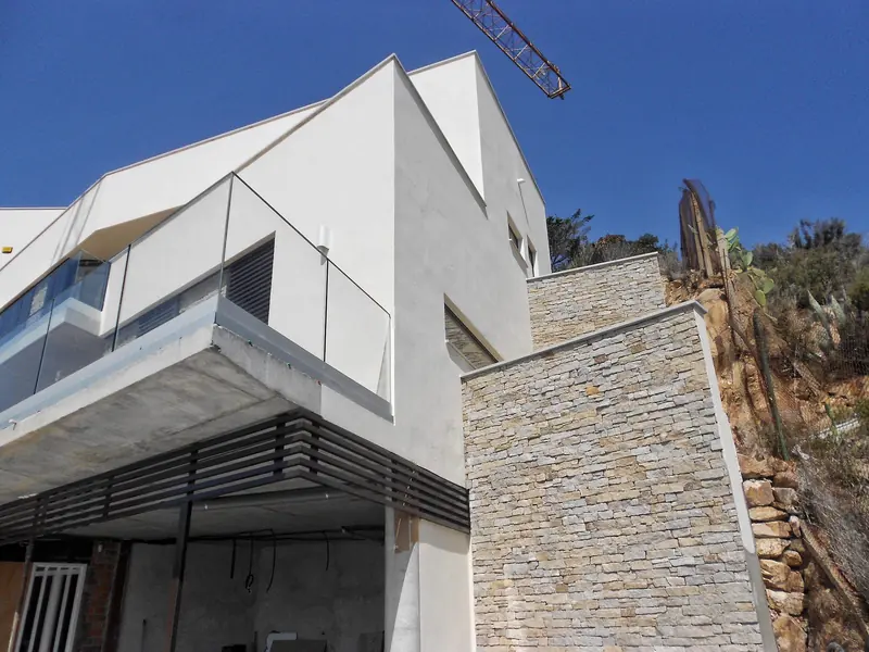 Habitatge en construcció amb volums blancs, aplacat de pedra i una grua al fons