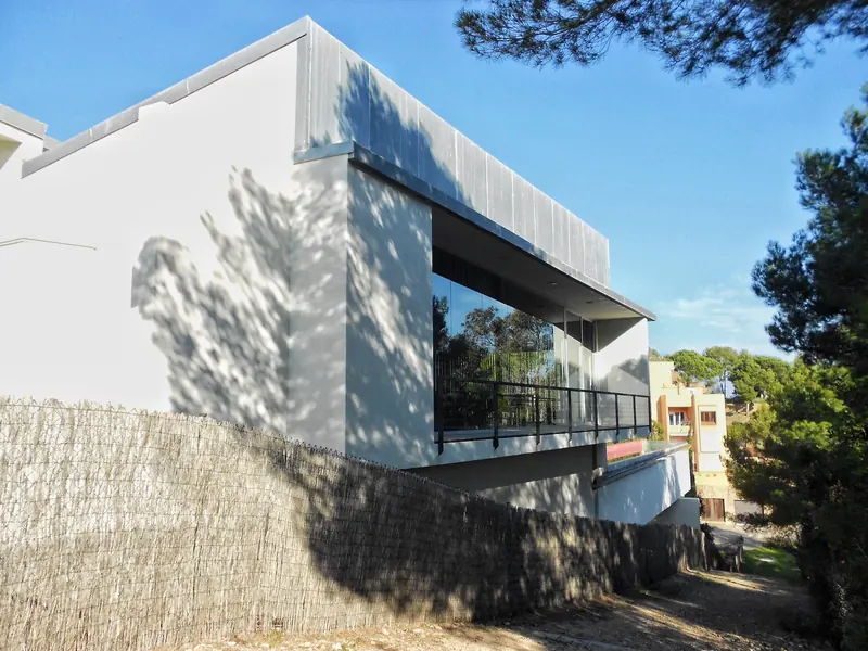 Habitatge contemporani de façana blanca amb un volum en voladís i balcó de vidre entre pins