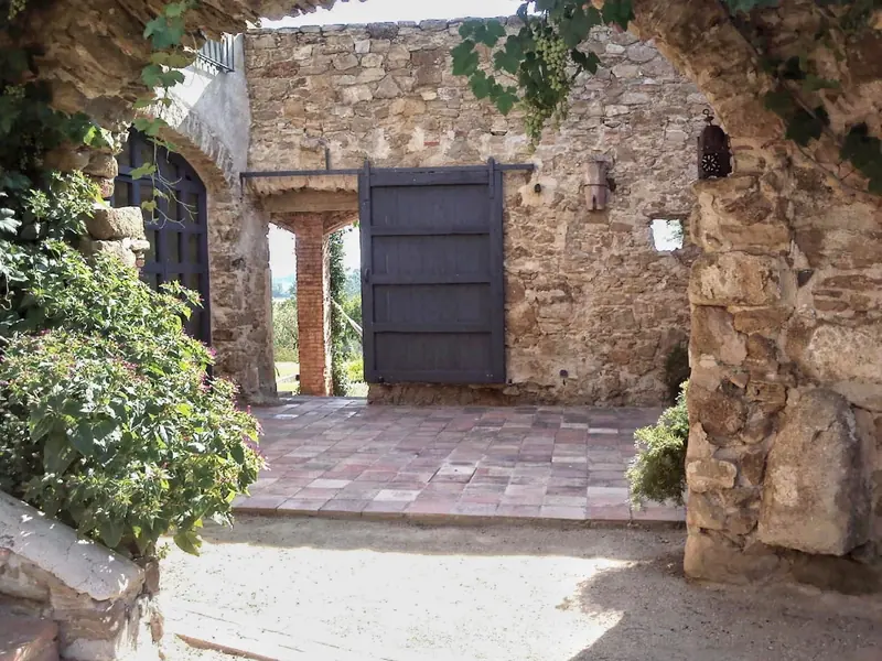 Pati d’entrada d’una casa de pedra amb portalada de fusta i vegetació enfiladissa