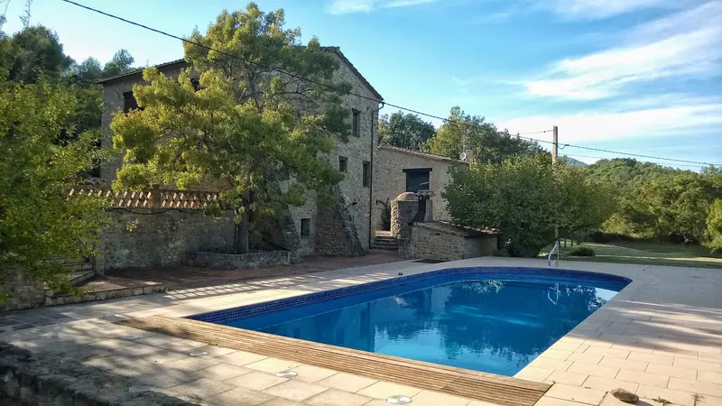 Piscina davant d’una masia de pedra envoltada de vegetació