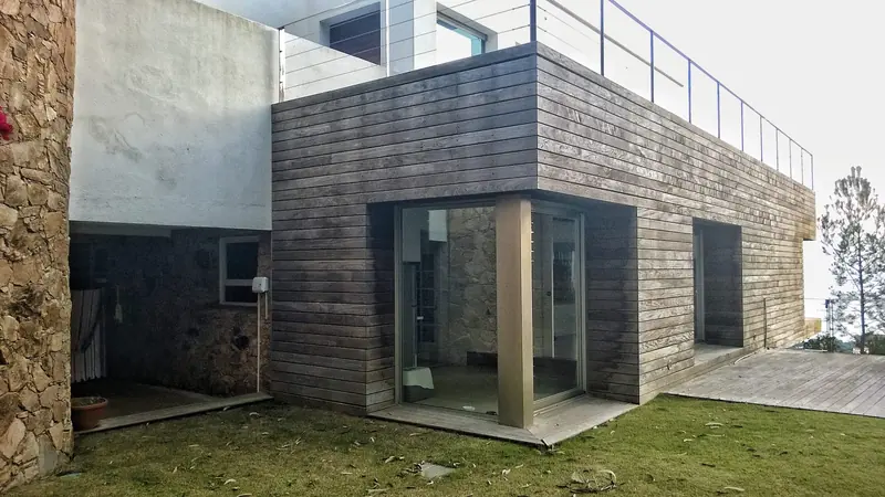 Volum revestit de fusta amb porta de vidre i terrassa superior amb barana