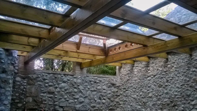 Pèrgola de fusta amb coberta de vidre sobre un mur de pedra