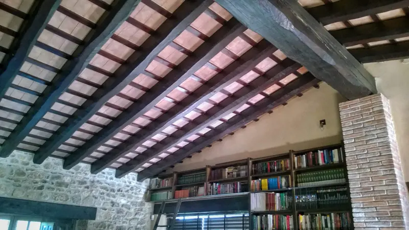 Interior amb sostre de bigues de fusta, paret de pedra i una llibreria