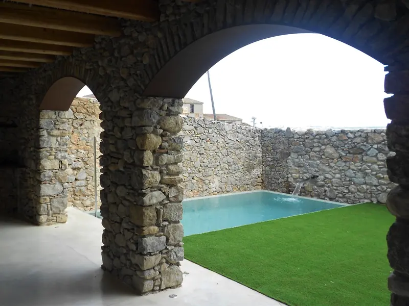 Arcs de pedra d’un porxo que donen a una piscina amb gespa