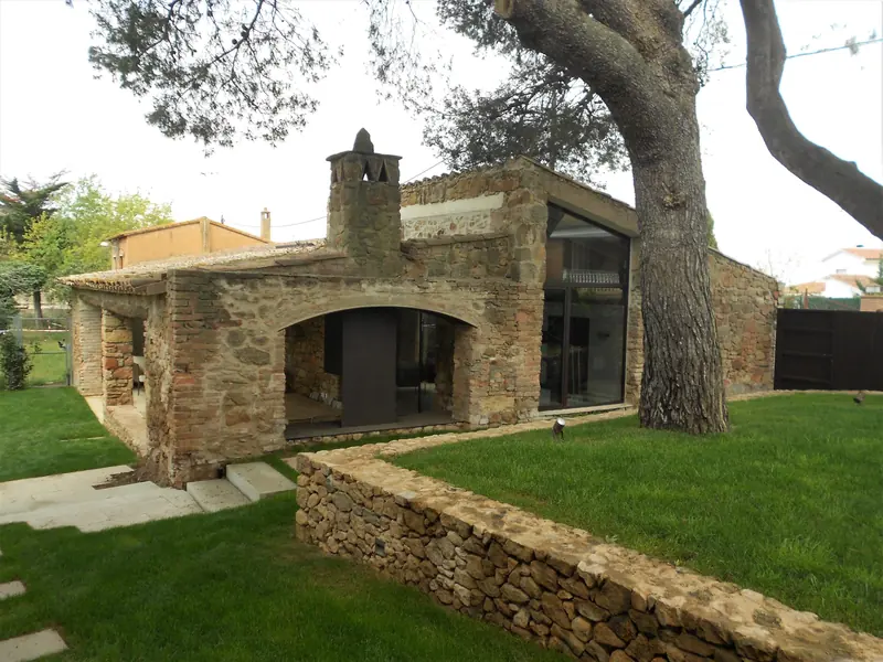 Construcció de pedra rehabilitada sota un pi, amb finestral, xemeneia i jardí